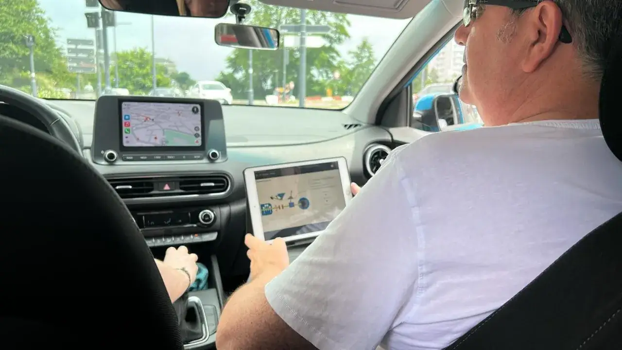 Un homme utilise une tablette pour surveiller le système d'un véhicule pendant la conduite. L'écran du GPS est également visible.
